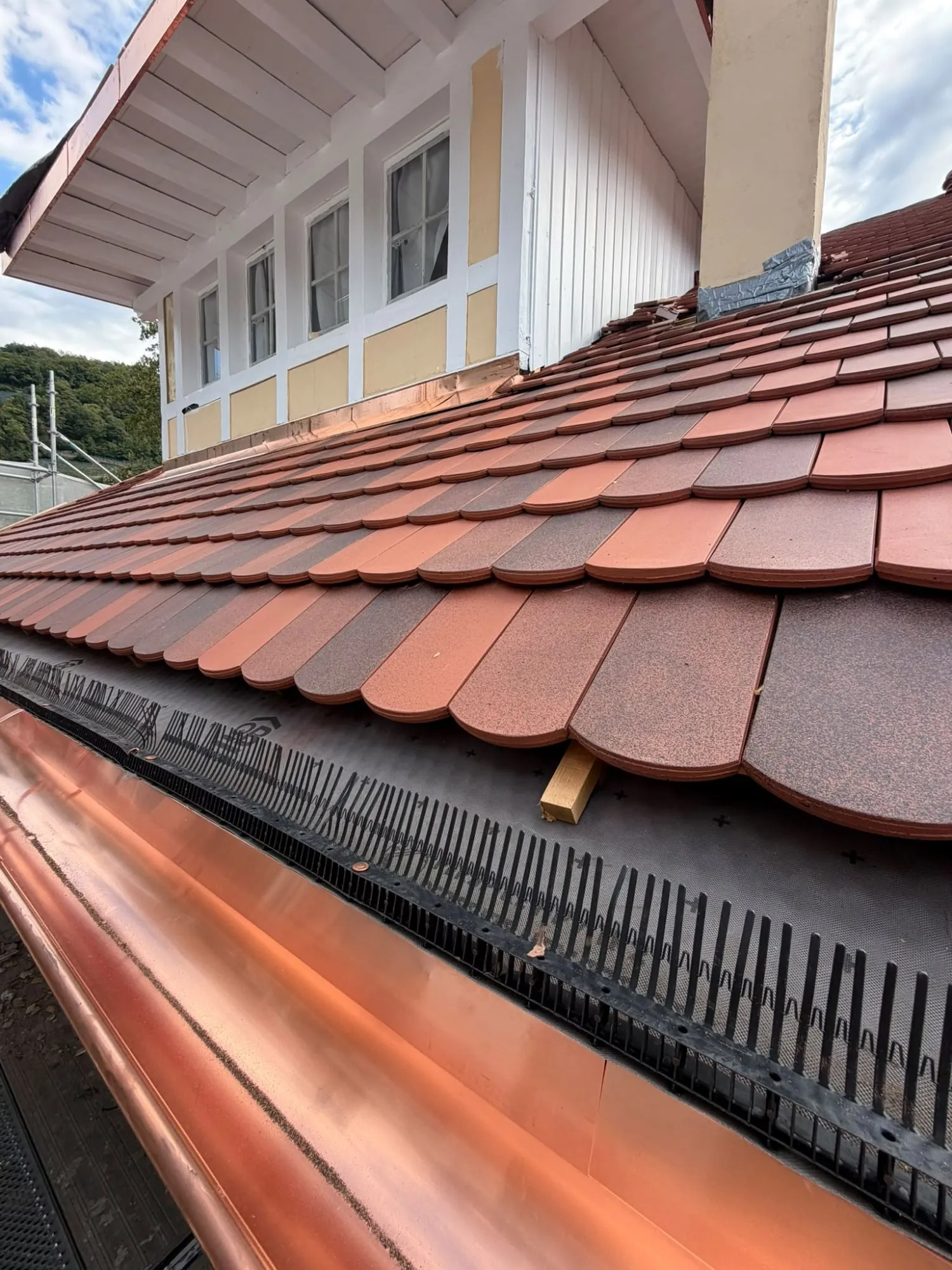 Pose de tuiles plates en terre cuite et gouttière en cuivre à l’égout d’une toiture